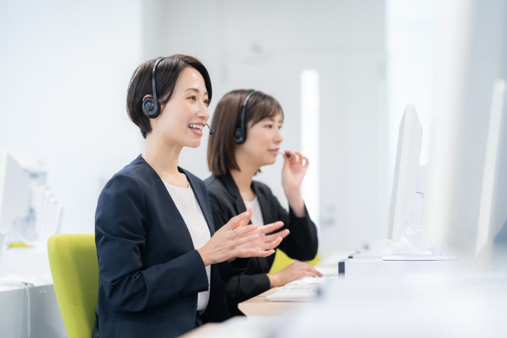 ヘッドセットを着けてパソコンに向かい、手ぶりを交えて通話する女性2名