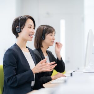 ヘッドセットを着けてパソコンに向かい、手ぶりを交えて通話する女性2名