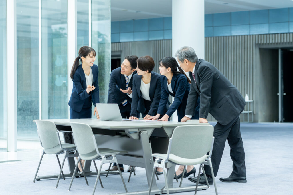 会議室のテーブルを囲み資料とノートパソコンで営業プロセスを検討する社員たち