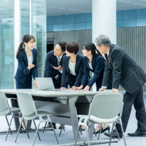 会議室のテーブルを囲み資料とノートパソコンで営業プロセスを検討する社員たち