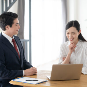 ノートPCの画面を一緒に見ながら商談する男性の営業担当者とミドル世代の女性
